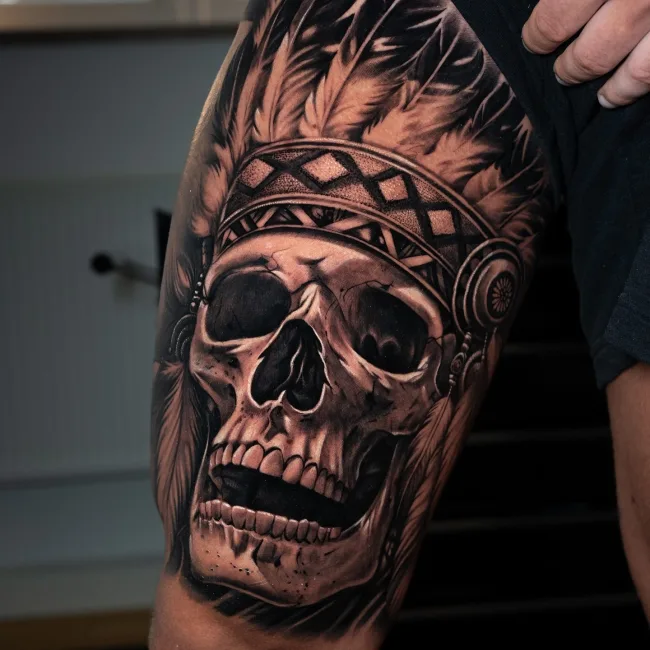 Black and Grey Totenkopf mit Federschmuck am Oberschenkel – Chema, Prime Ink Bremen